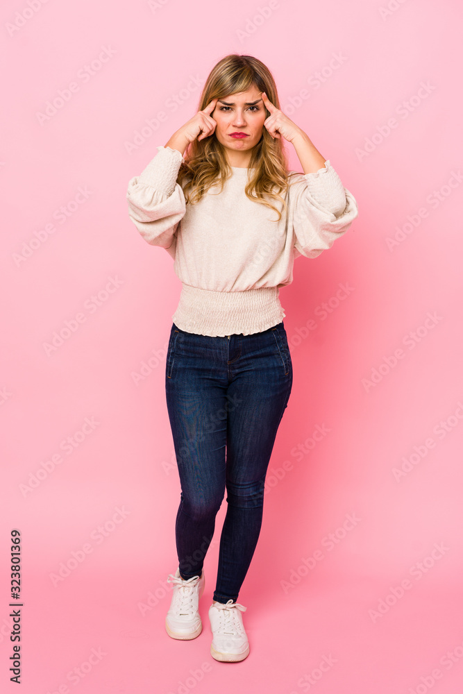 Young blonde caucasian woman standing over a pink background focused on a task, keeping forefingers pointing head. Young blonde caucasian woman standing over a pink background focused on a task, keeping forefingers pointing head.