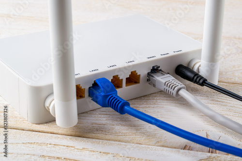 Close-up of network cables connected to a white Wi-Fi wireless router on a white wooden table. Wlan router with internet cables plugged in on a table in a home or office.