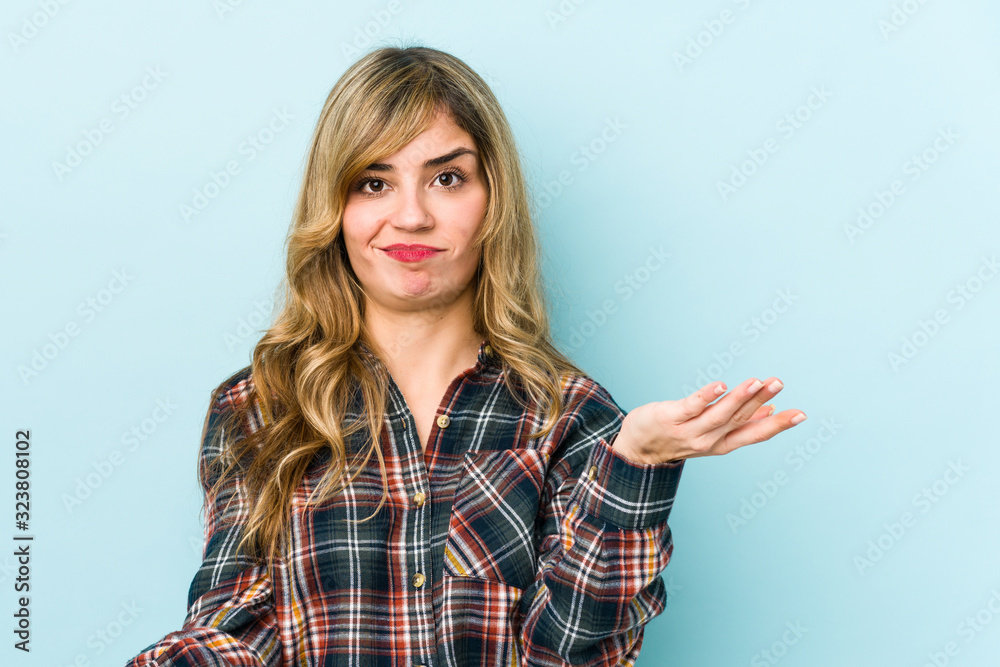 Young blonde caucasian woman makes scale with arms, feels happy and confident.