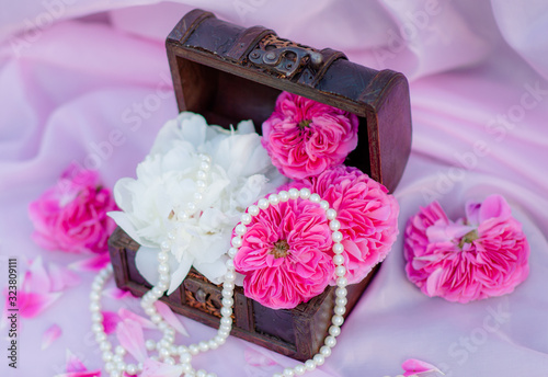 Floral arrangement of pink roses flowers and peonies in a wooden box with pearl beads on a pink background. Flat lay of wedding decorations and decorations. Floristically photo