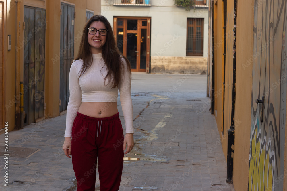 attractive young woman model smiling with eyeglasses, in the city, white top and red pants, dark air. Place for your text in copy space.