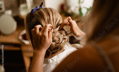 Morning hairstyle preparation of bride with hands of hairdresser. Focus on the detail of the groomed hair. Background and foreground slightly blurred.