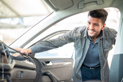 Smiling man taking taking look to car in showroom