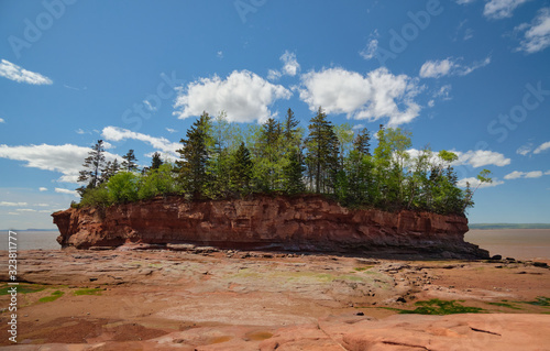 Red flowerpot formation at Burntcoat Head Park at lower tide. Green trees and grass on the top. Blue cloudy sky on the background.