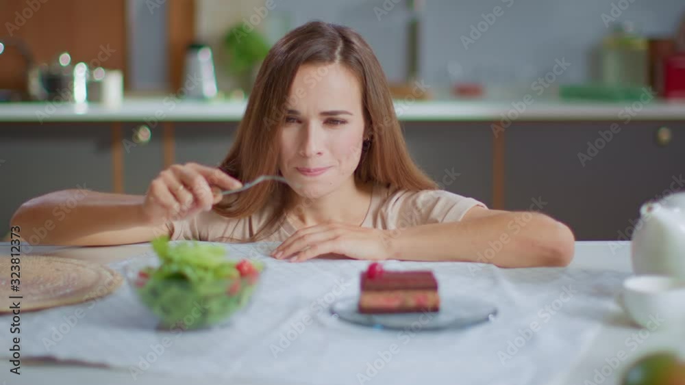 Attractive woman choosing between salad and cake on table. Healthy food concept Attractive woman choosing between salad and cake on table. Healthy food concept