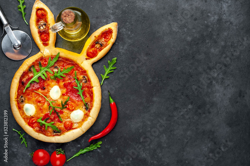 Easter pizza in the form of a hare with eggs, tomatoes, sunflower oil on a stone background with copy space for your text