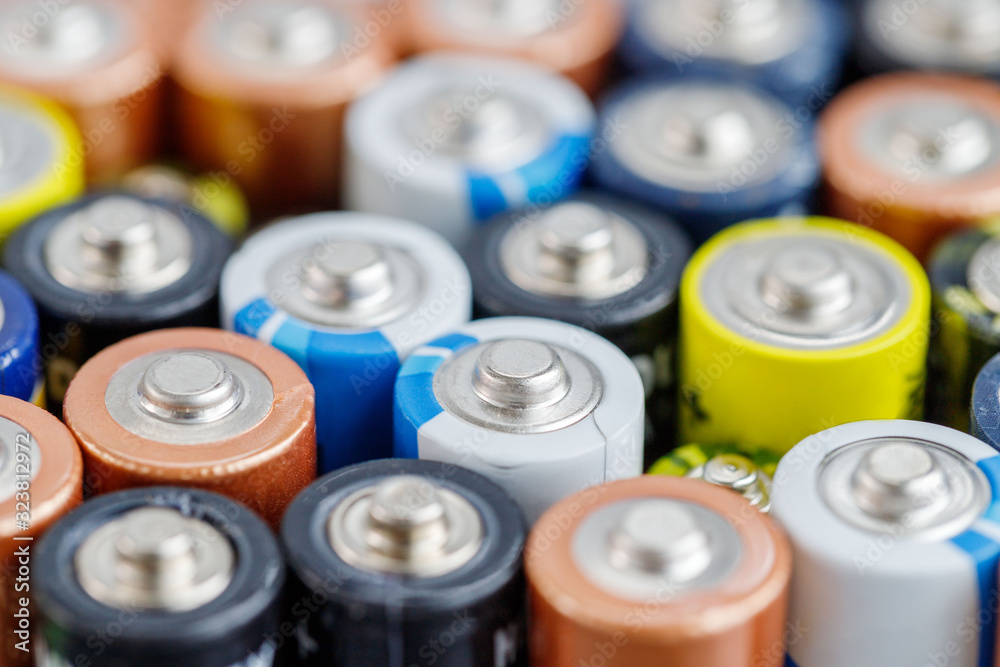 Close up of positive ends of colorful  discharged batteries of different sizes and formats, top view, selective focus. Used alkaline battery. Hazardous garbage concept