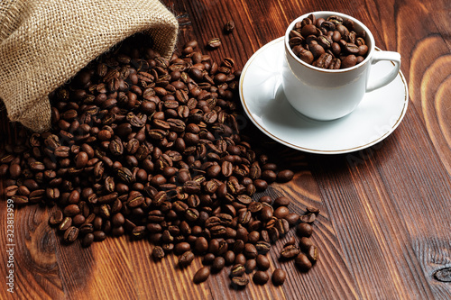 Roasted coffee beans on a wooden background with next to a white cup. Fresh drink.