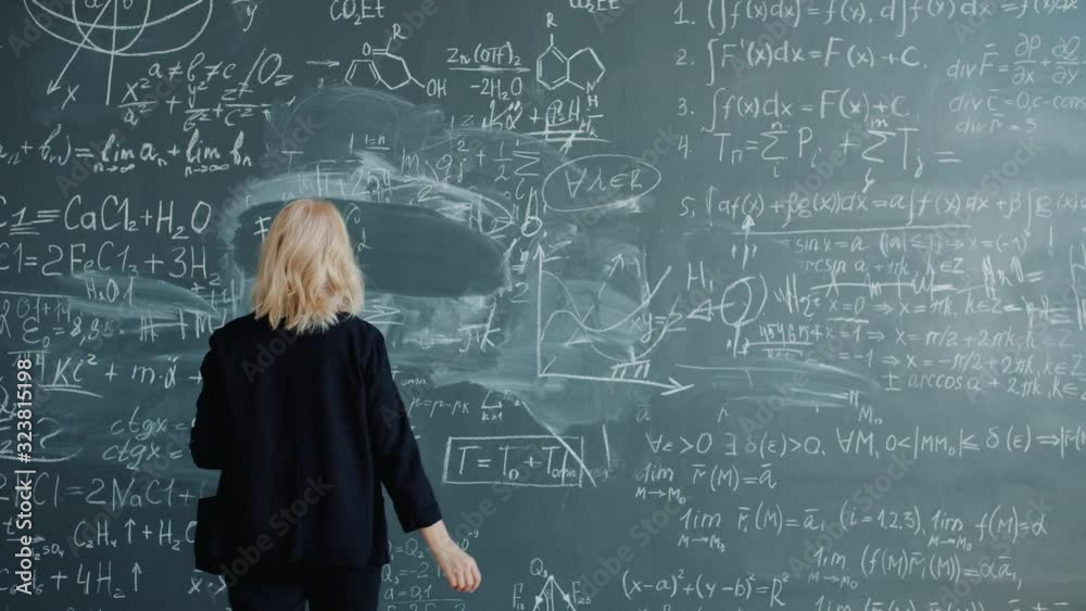 Back view of female scientist walking to chalkboard writing formulas with chalk concentrated on science. Occupation, intelligent people and knowledge concept.