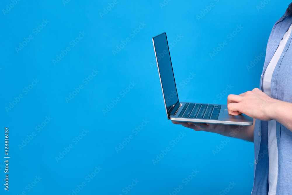 A man in a blue shirt is holding a laptop. Concept of student learning material on the Internet. Copy space. A man in a blue shirt is holding a laptop. Concept of student learning material on the Internet. Copy space.