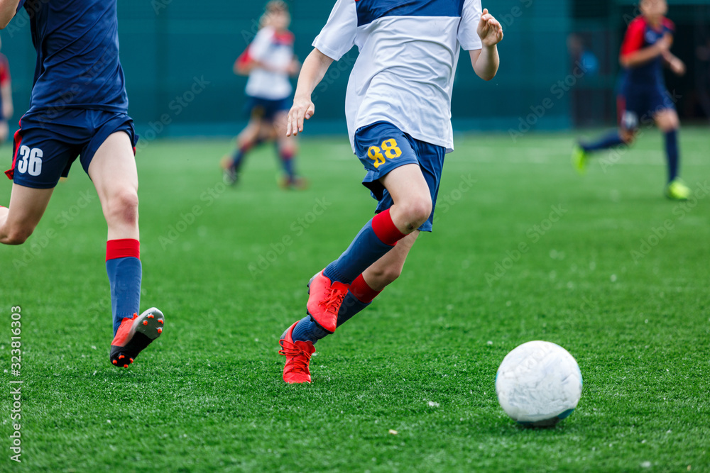 Boys in white and blue sportswear plays football on field, dribbles ball. Young soccer players with ball on green grass. Training, football, active lifestyle for kids concept Boys in white and blue sportswear plays football on field, dribbles ball. Young soccer players with ball on green grass. Training, football, active lifestyle for kids concept