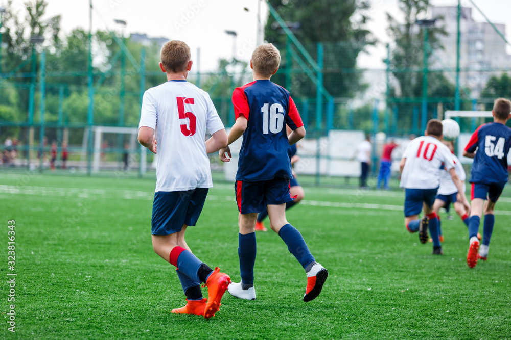 Boys in white and blue sportswear plays  football on field, dribbles ball. Young soccer players with ball on green grass. Training, football, active lifestyle for kids concept 