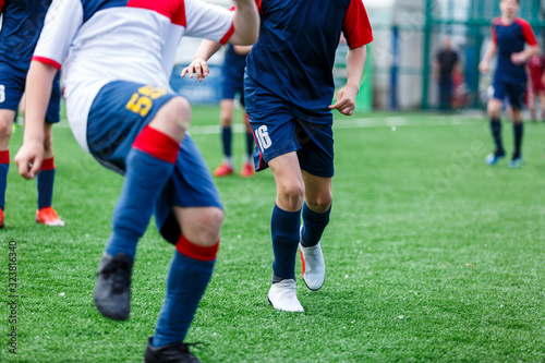 Boys in white and blue sportswear plays football on field, dribbles ball. Young soccer players with ball on green grass. Training, football, active lifestyle for kids concept 