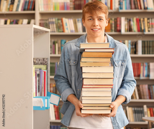 Portrait of male student with big stack of books in library