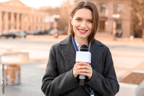 Beautiful journalist with microphone outdoors photo