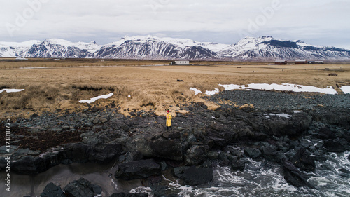 young male traveler in green clothes in a red hat and a green backpack walks along the path against the background of mountains in Iceland