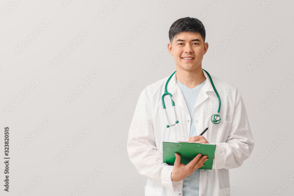 Male Asian doctor with clipboard on light background Male Asian doctor with clipboard on light background