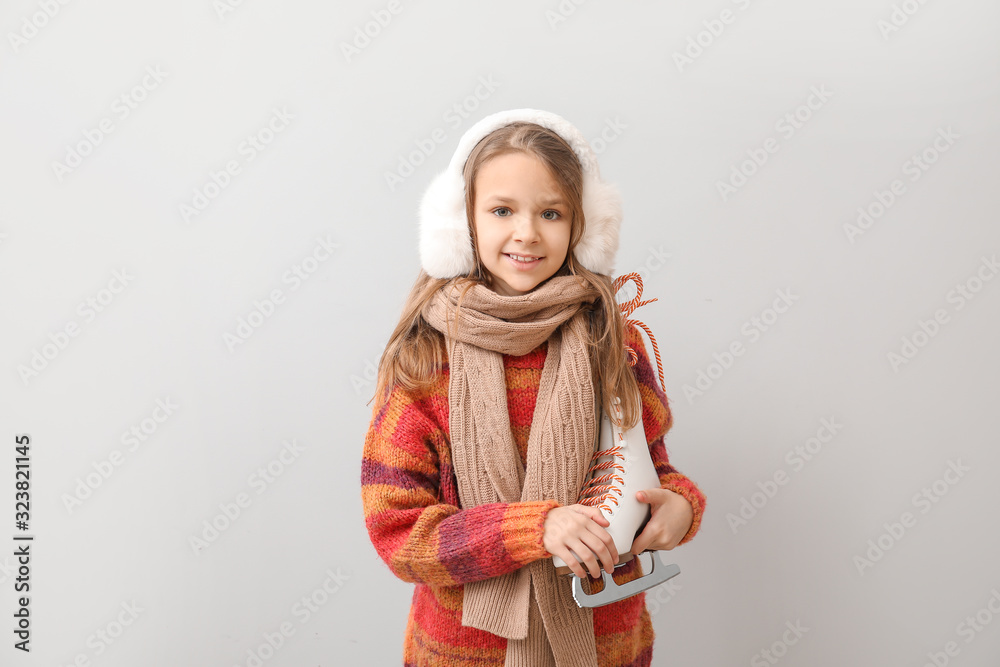 Cute little girl with ice skates on light background