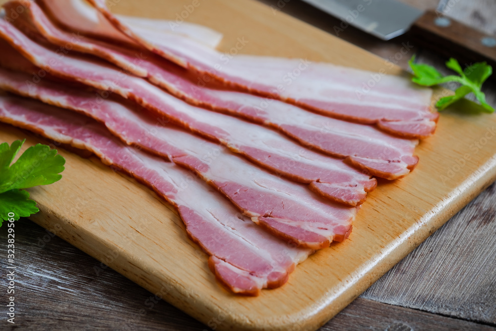 Raw sliced bacon on wooden board.