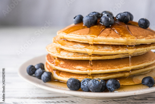 Close up of fluffy pancakes with maple syrup and blueberries against white wooden background