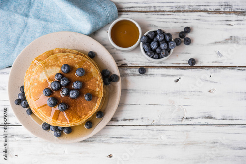 Close up of fluffy pancakes with maple syrup and blueberries against white wooden background
