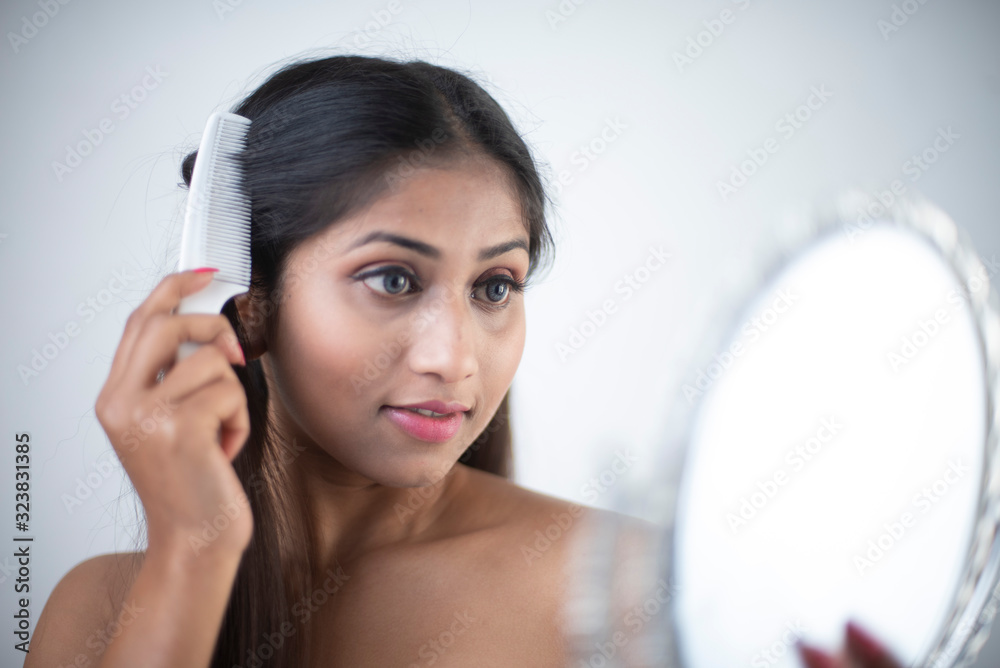 Fashion portrait of an Asian/Bengali/Indian brunette woman combing her hair looking at the mirror in white background. Indian lifestyle and fashion photography. Fashion portrait of an Asian/Bengali/Indian brunette woman combing her hair looking at the mirror in white background. Indian lifestyle and fashion photography.