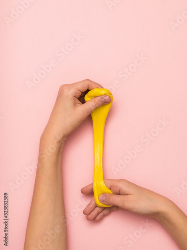 Children's hands stretch a thin bright yellow slime on a pink background.