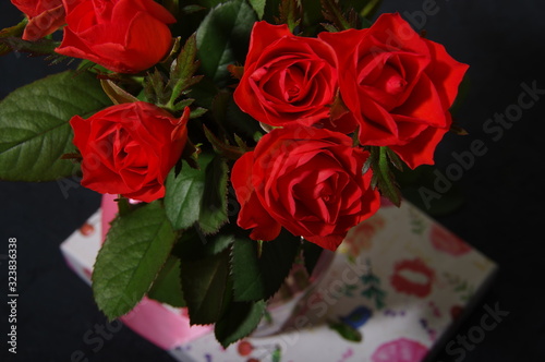 Bouquet red roses flower in glass vase on dark background and gift box, top view