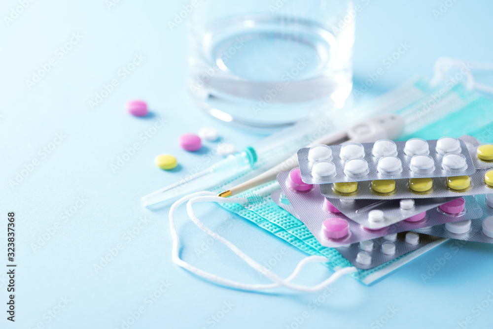 Concept of therapy, prevention of virus flu, viral attack, colds pills, antibiotics and vitamins, protective medical face masks over blue background. Coronavirus Covid-19. Copy space Concept of therapy, prevention of virus flu, viral attack, colds pills, antibiotics and vitamins, protective medical face masks over blue background. Coronavirus Covid-19. Copy space