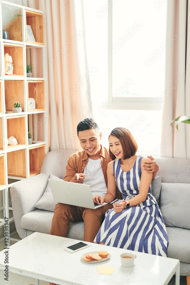 Φωτογραφία Young Asian couple buying online or paying bills by credit card with laptop at h