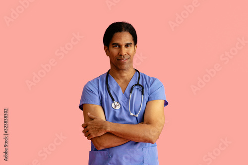 Studio portrait of a friendly male doctor or nurse wearing blue scrubs and stethoscope and arms crossed