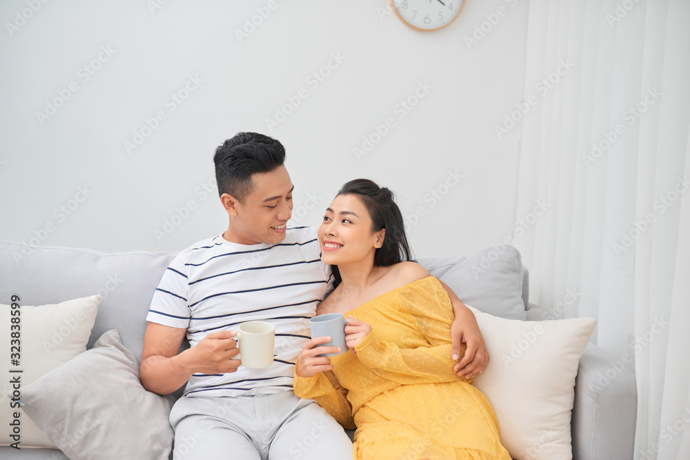 Couple in love enjoying their free time, sitting on a couch,drinking coffee and chatting.
