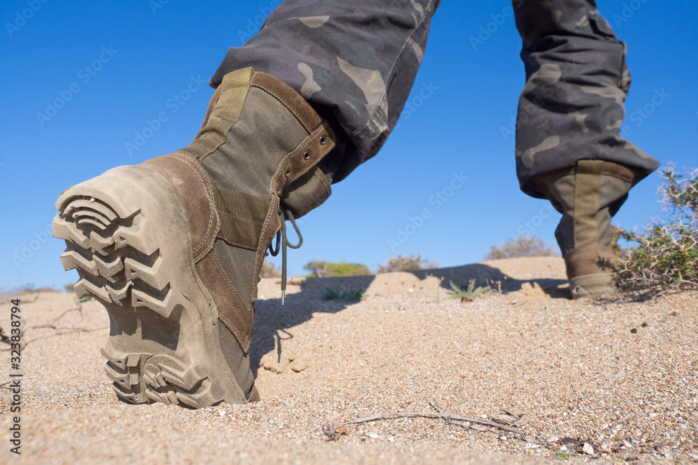 Human feet in hiking rough boots stepping on the sand in a desert, close up, wide angle, selected focus