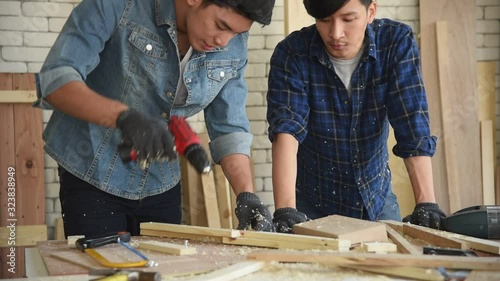 Young Asian group man carpenter worker using electric hand drill to build diy wood furniture in workshop