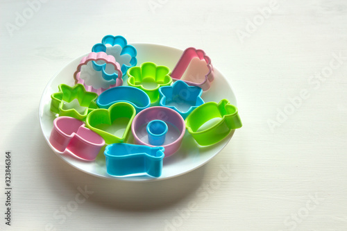 multi-colored plastic cookie cutters are in a white bowl on a white table