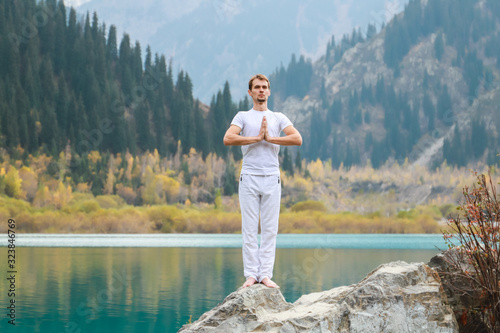 A young man in white practices yoga in the mountains. Pose Samasthiti namaskar photo