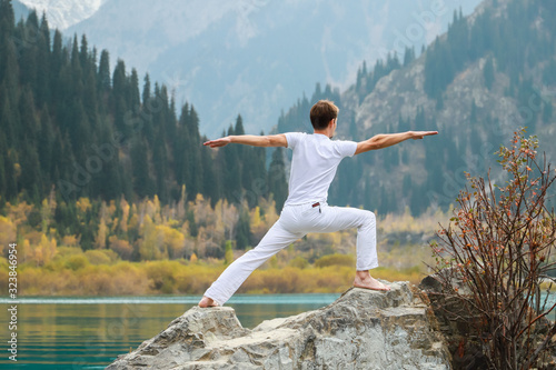 A man practices yoga on a background of mountains. Pose Virabhadrasana 2 or warrior