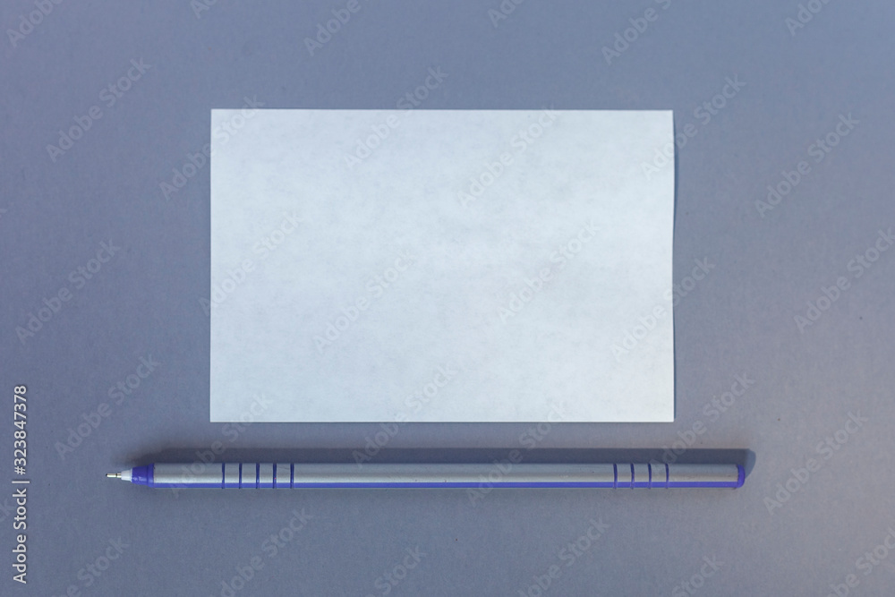 Empty paper piece of white paper and a pen in the center of the grey background. Copy space, negative space for ad and text. Top view Empty paper piece of white paper and a pen in the center of the grey background. Copy space, negative space for ad and text. Top view