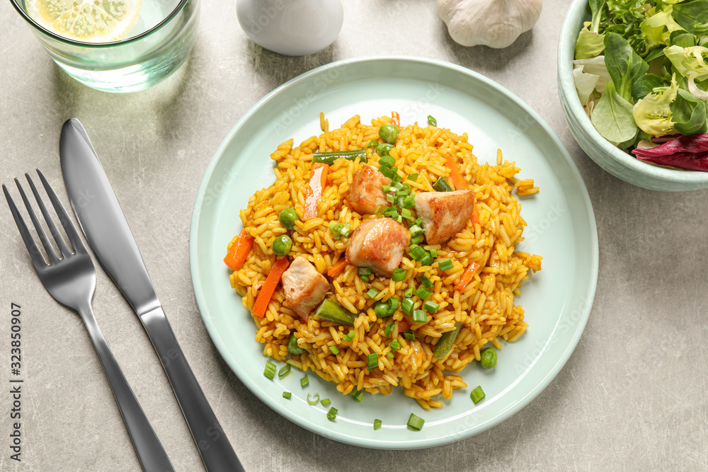 Delicious rice pilaf with vegetables and chicken served on light grey table, flat lay