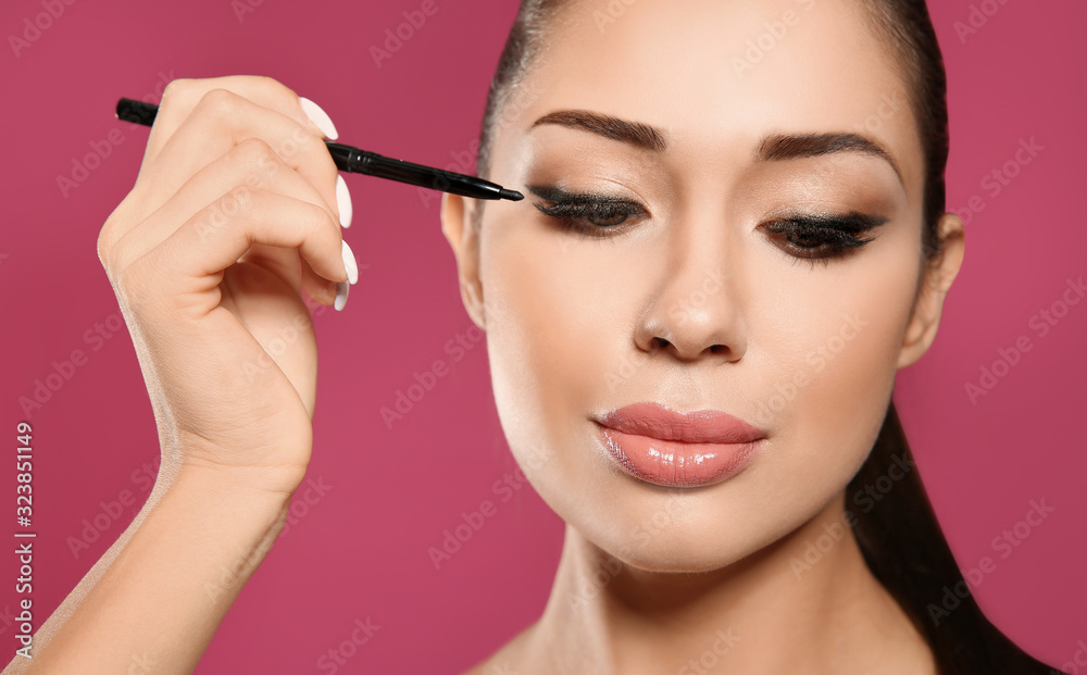 Beautiful woman applying eyeliner on pink background, closeup. Stylish makeup