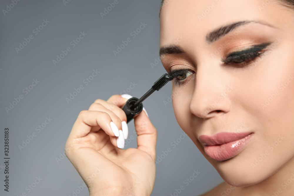 Beautiful woman applying mascara on light grey background, closeup. Stylish makeup Beautiful woman applying mascara on light grey background, closeup. Stylish makeup