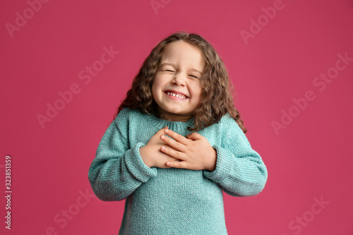 Cute grateful little girl with hands on chest against pink background photo