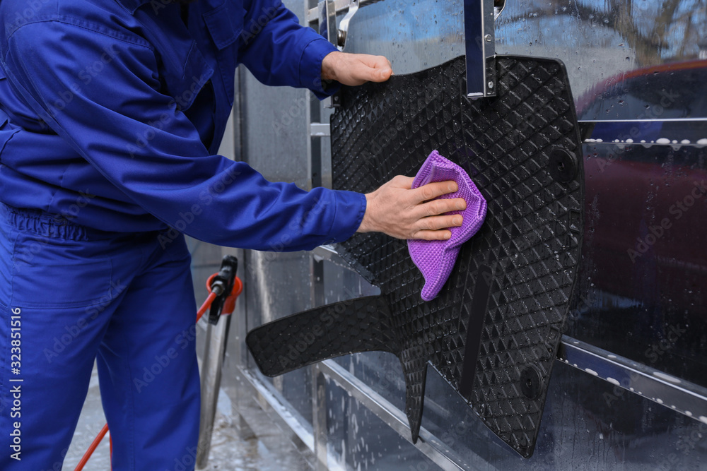 Worker wiping automobile floor mat at car wash, closeup