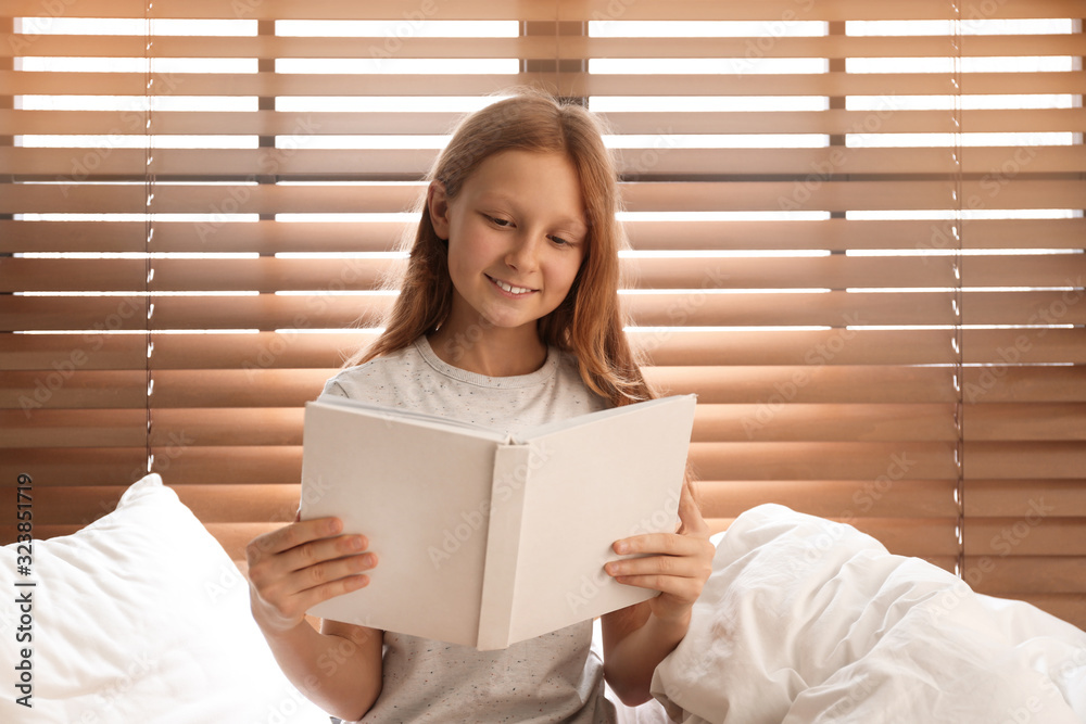 Cute preteen girl reading book on bed near window Stock Photo | Adobe Stock
