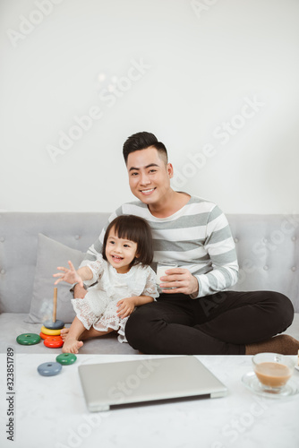 Father giving milk for his daughter when they sitting on sofa at home.