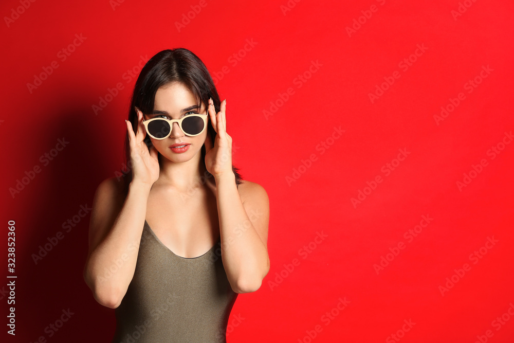 Beautiful woman in stylish swimsuit and sunglasses on red background. Space for text
