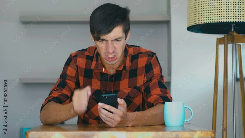 Angry Man Using Mobile phone at home. Frustrated entrepreneur is angry with the message that he read in the smartphone. Stressed businessman uses smartphone.