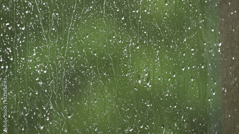 Rain drops running down the window surface. Heavy summer rain outside. Strong wind and rain drops falling on glass window in the balcony. Dramatic thunder storm outside