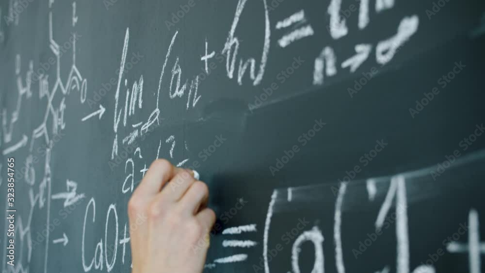 Close-up of male hand writing mathematics equations on chalkboard in class, mathematician is busy with calculations. People and education concept.