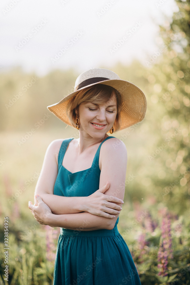Beautiful romantic woman blonde in a dress and hat in a field of purple flowers of lupins at dawn. Soft selective focus.